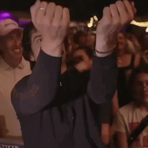 A Man Is Holding His Hands Up In The Air While A Crowd Watches GIF