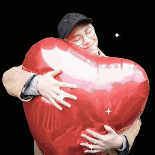 A Man Is Hugging A Heart Shaped Balloon With The Letter P On His Hat GIF