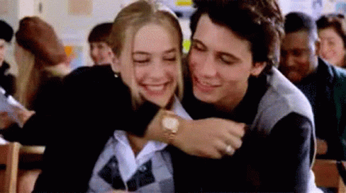 A Man Is Hugging A Woman In A Classroom In Front Of A Crowd Of People . GIF
