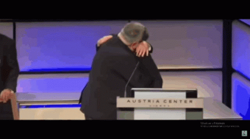 A Man Is Hugging Another Man In Front Of A Podium That Says Austria Center GIF