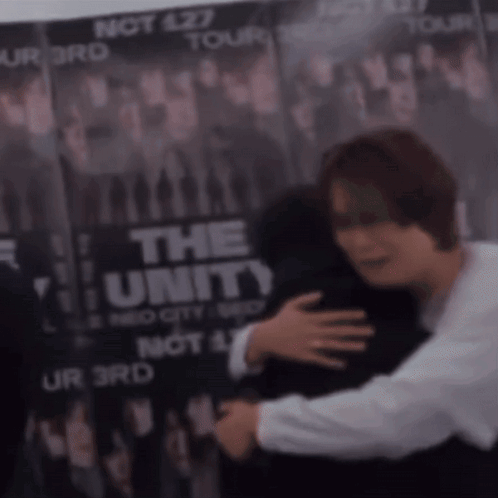 A Man Is Hugging Another Man In Front Of A Poster That Says The Unity GIF