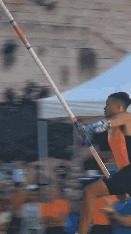 A Man Is Jumping A Pole In Front Of A Crowd Of People GIF