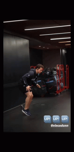 A Man Is Jumping In The Air In A Gym With A Sign That Says Up GIF