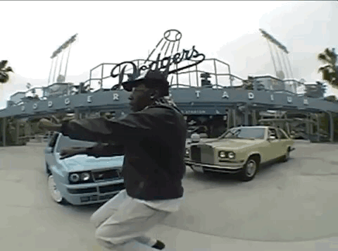 A Man Is Jumping In The Air In Front Of Dodgers Stadium GIF