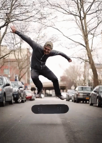 A Man Is Jumping In The Air With A Skateboard In The Foreground GIF