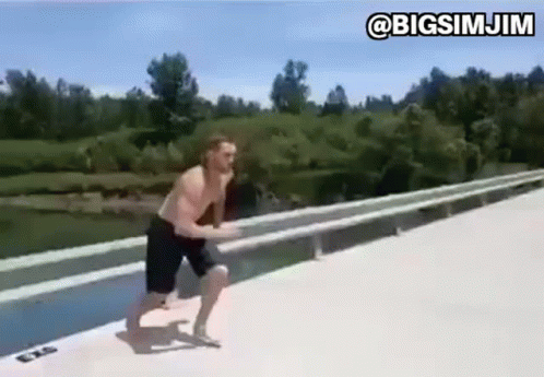A Man Is Jumping Into A Body Of Water From A Bridge . GIF