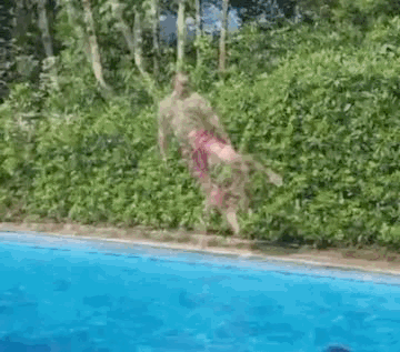 a man is jumping into a swimming pool with trees in the background .