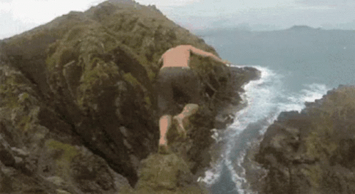 A Man Is Jumping Off A Cliff Into The Ocean . GIF