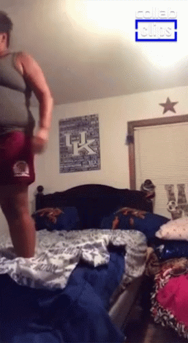 A Man Is Jumping On A Bed With A Uk Poster On The Wall GIF