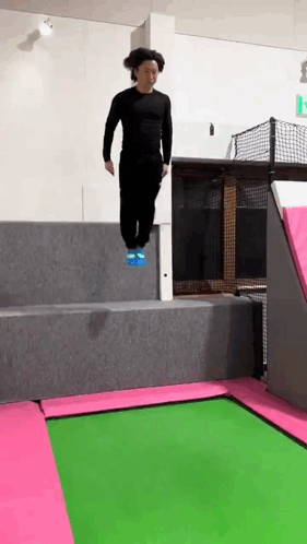 A Man Is Jumping On A Trampoline With A Pink And Green Mat . GIF