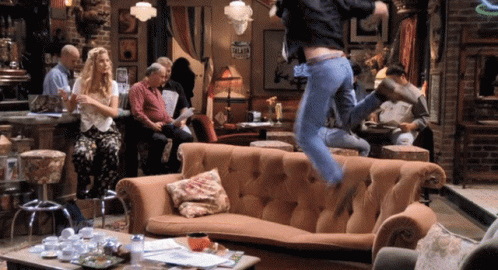 A Man Is Jumping Over A Couch In A Room With A Sign That Says " Valet " On It GIF