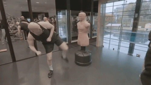A Man Is Kicking A Punching Bag In A Gym While Another Man Watches GIF