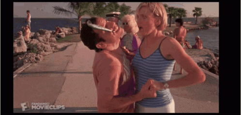 A Man Is Kissing A Woman On The Cheek While Standing On A Beach . GIF