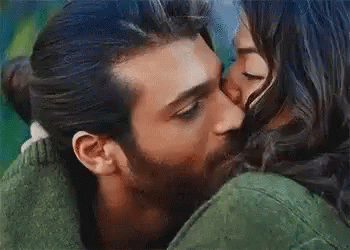 A Man Is Kissing A Woman On The Cheek While They Are Hugging . GIF