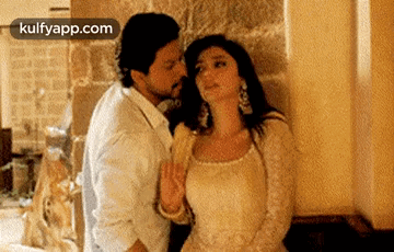 A Man Is Kissing A Woman On The Neck In Front Of A Wall . GIF