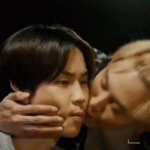 A Man Is Kissing Another Man On The Cheek In A Dark Room . GIF