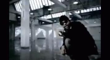 A Man Is Kneeling Down In A Dark Room With A Gun . GIF