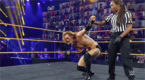a man is kneeling down in a wrestling ring with a referee standing behind him .