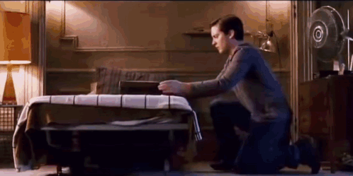 A Man Is Kneeling Down In Front Of A Bed In A Bedroom . GIF