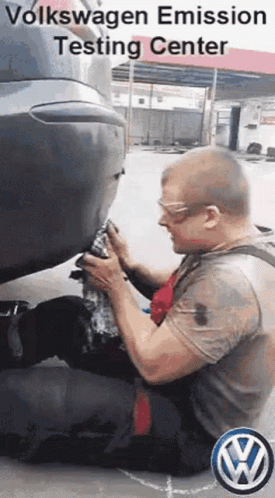 A Man Is Kneeling Down In Front Of A Volkswagen Car . GIF