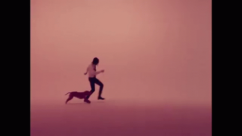 A Man Is Kneeling Down Next To A Small Dog In A Pink Background . GIF