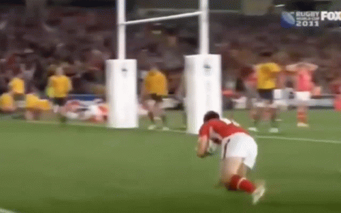 A Man Is Kneeling Down On A Soccer Field With A Rugby Ball . GIF