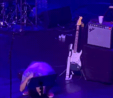 A Man Is Kneeling Down On A Stage With A Guitar Behind Him GIF