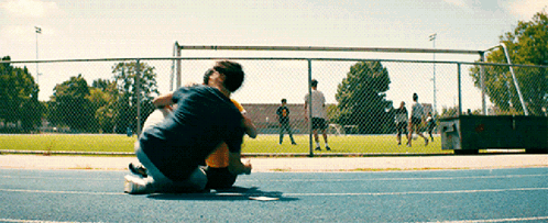 A Man Is Kneeling Down On A Track With A Child In His Lap GIF