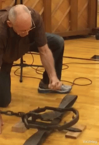 A Man Is Kneeling Down On A Wooden Floor Next To A Piano And A Snake Trap . GIF