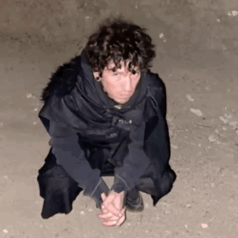 A Man Is Kneeling Down On The Ground With His Hands Folded . GIF