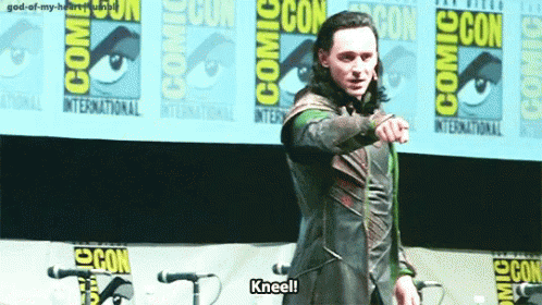 A Man Is Kneeling In Front Of A Comic Con Banner . GIF