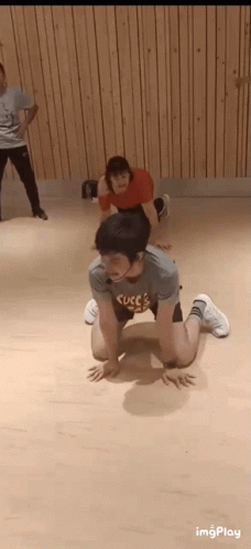 A Man Is Kneeling On The Floor In A Dance Studio While A Woman Stands Behind Him . GIF