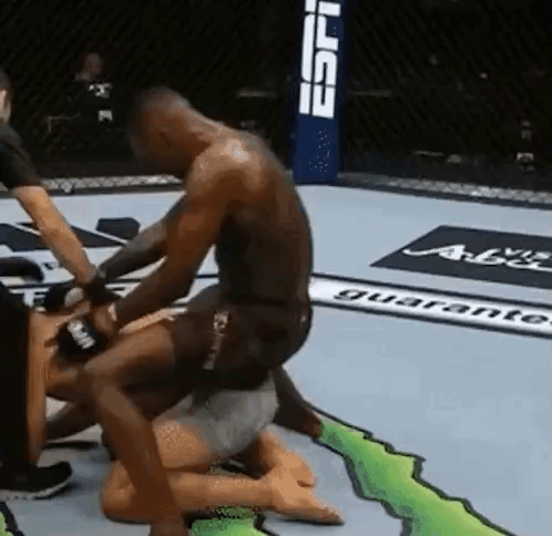 A Man Is Kneeling On Top Of Another Man In A Wrestling Ring . GIF