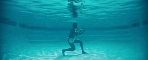 A Man Is Kneeling Underwater In A Swimming Pool . GIF