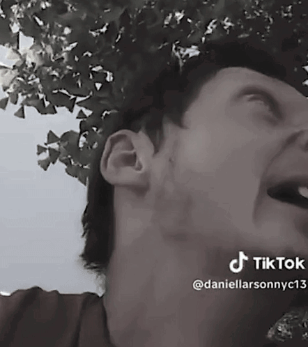 A Man Is Laughing In A Black And White Photo With A Tree In The Background . GIF