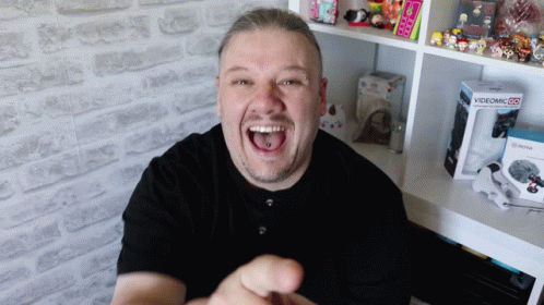 A Man Is Laughing In Front Of A Videomic Box On A Shelf GIF