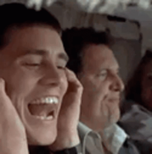 A Man Is Laughing On A Plane While Another Man Covers His Ears . GIF