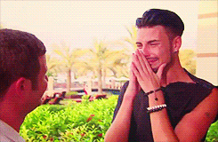 A Man Is Laughing While A Woman Covers His Mouth With Her Hands . GIF