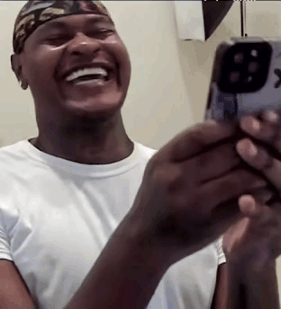 A Man Is Laughing While Holding A Cell Phone In His Hands . GIF
