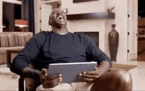 A Man Is Laughing While Holding A Tablet In His Hands . GIF