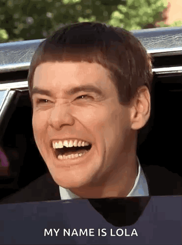 A Man Is Laughing While Sitting In A Car With The Words " My Name Is Lola " Below Him GIF
