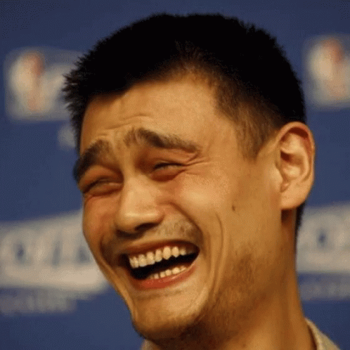 A Man Is Laughing With His Eyes Closed In Front Of A Nba Sign GIF