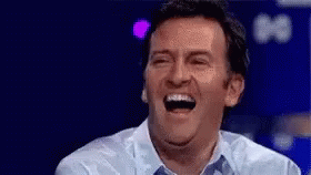 A Man Is Laughing With His Mouth Open While Wearing A Blue Shirt . GIF