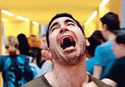 A Man Is Laughing With His Mouth Wide Open In A Crowd Of People . GIF