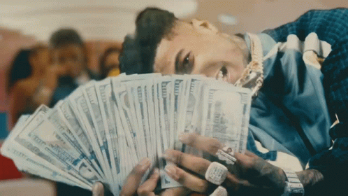 A Man Is Laying Down Holding A Fan Of Money In His Hands GIF