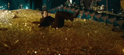 A Man Is Laying Down In A Pile Of Gold Coins . GIF