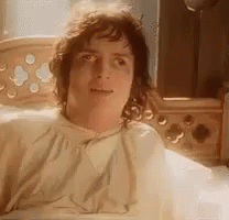 A Man Is Laying In A Bed With A Blanket On His Head And Looking At The Camera . GIF