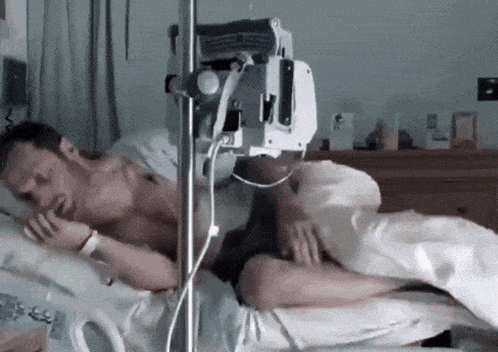A Man Is Laying In A Hospital Bed With An Iv In His Arm GIF