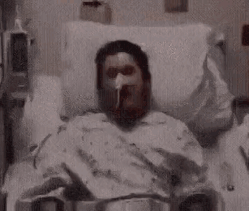 A Man Is Laying In A Hospital Bed With An Oxygen Mask On . GIF