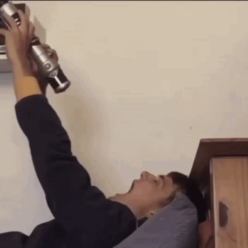 A Man Is Laying On A Bed Holding A Green Lightsaber GIF
